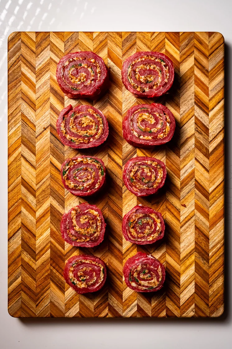 Нарезанные мясные рулеты на рабочей поверхности доски ЁЛОЧКА